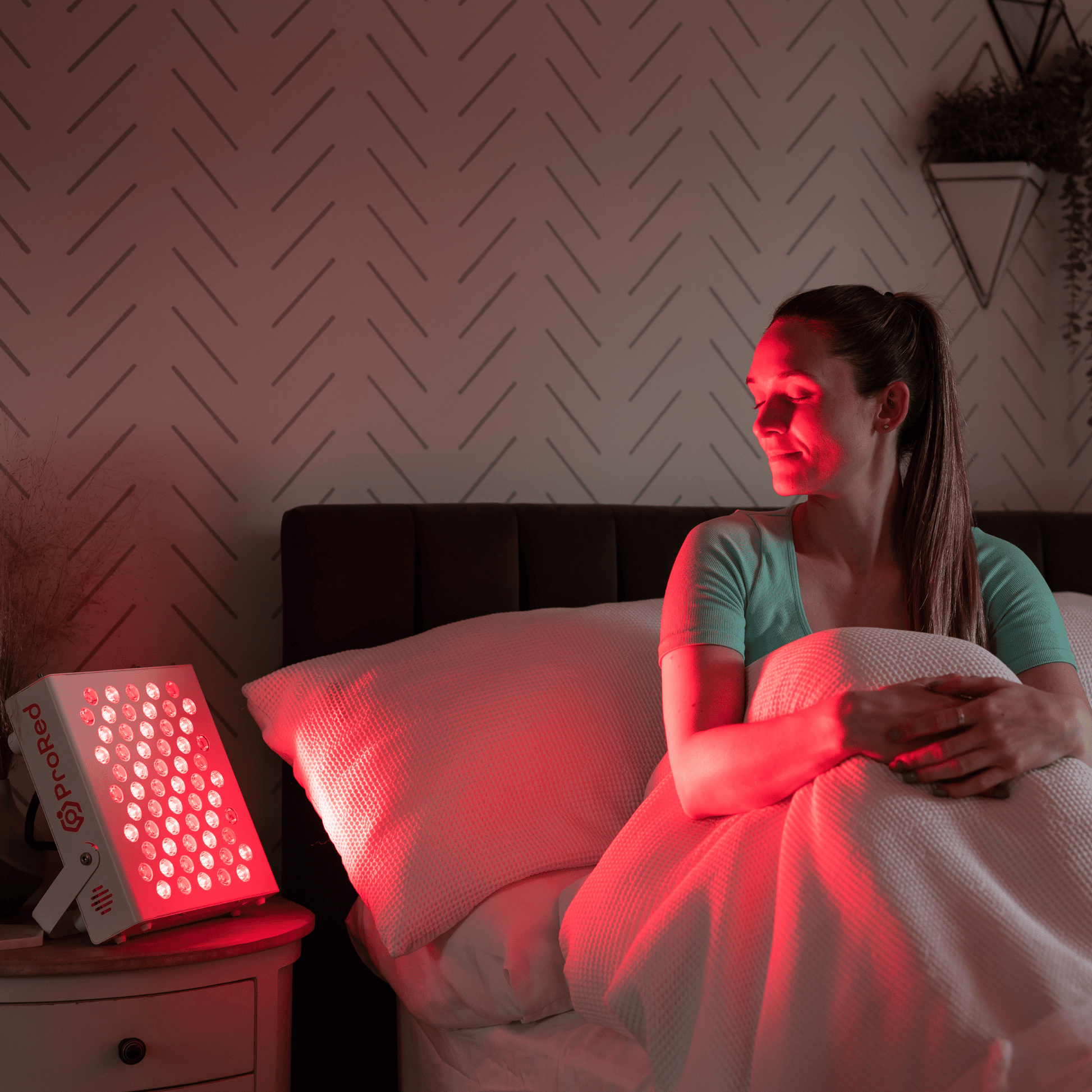 Girl sat in bed doing red light therapy with targeted device